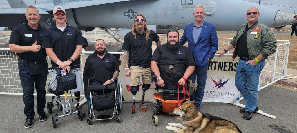 A wounded veterans team with Scott after event, fighter jet behind them