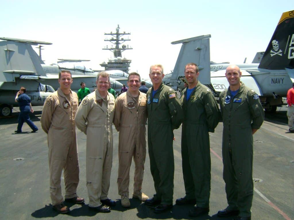 Scott with a Navy team on an aircraft carrier, several jets behind them