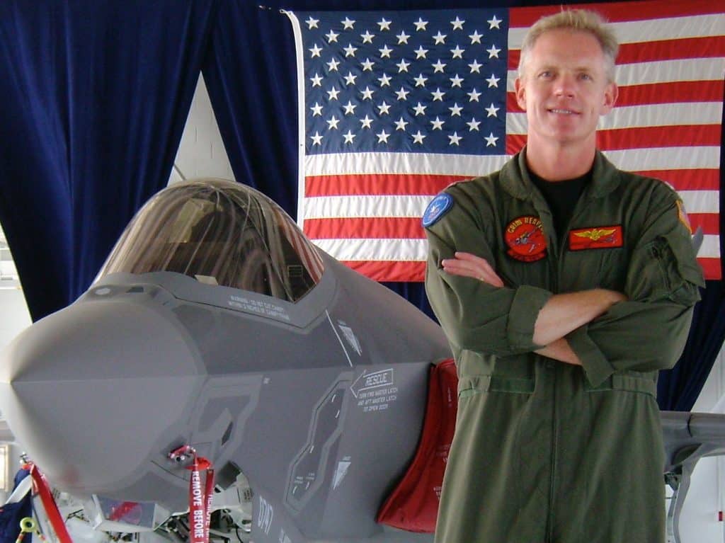 Scott Kartvedt with fighter jet and American flag behind him