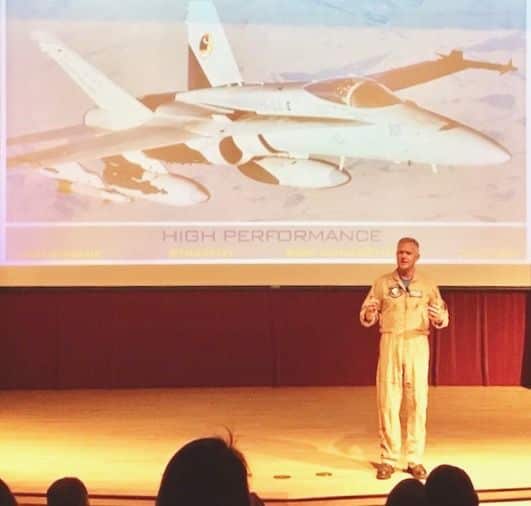 Scott Kartvedt on stage with large photo of fighter jet behind him